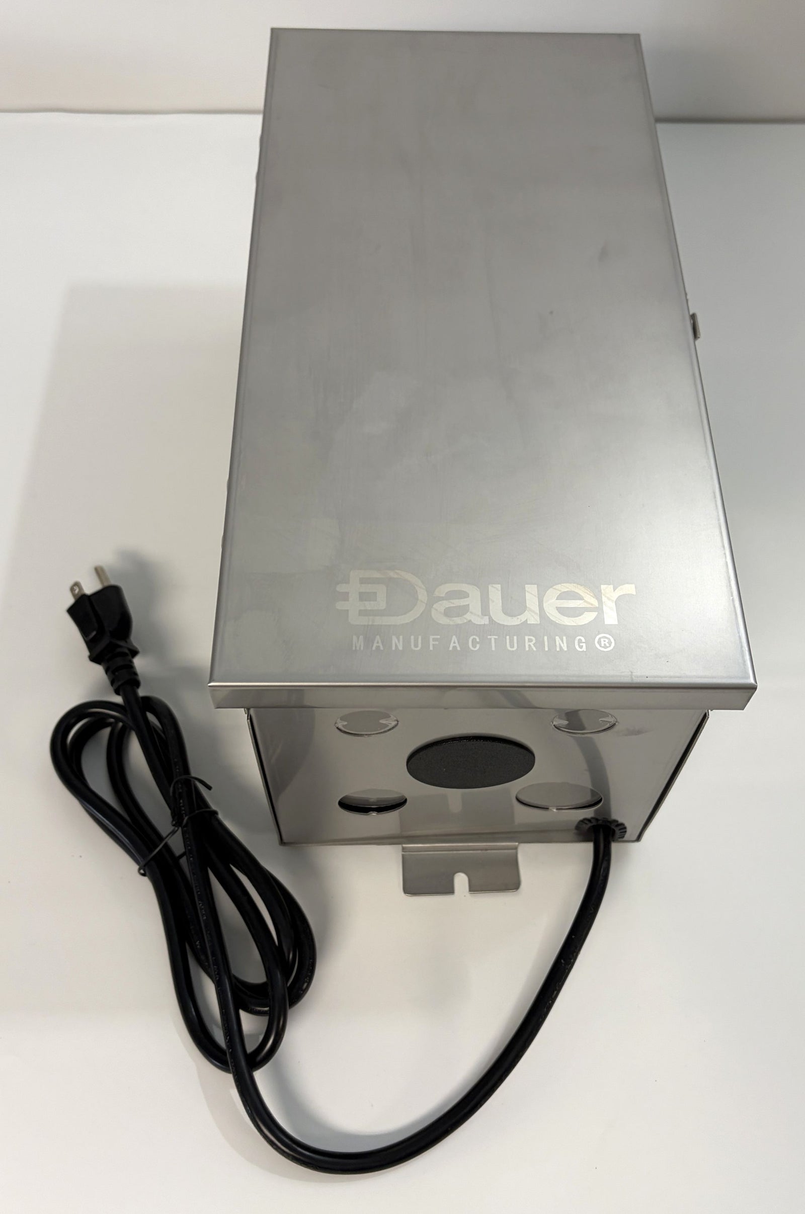 Stainless steel electrical transformer box with perforated sides, branded by Dauer Manufacturing, featuring attached power cord and grounded plug for landscape lighting applications.