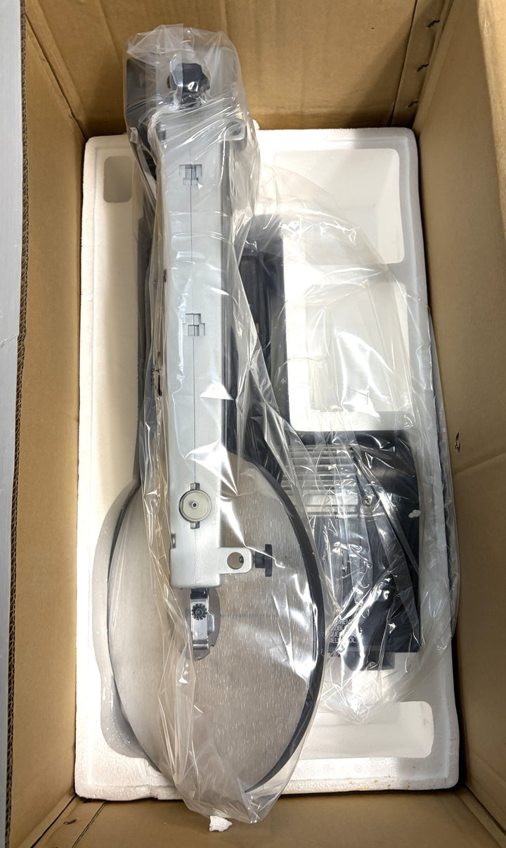 Partially assembled Dremel scroll saw with metal frame and black base, carefully packaged in plastic and secured within protective white foam inside a cardboard box.