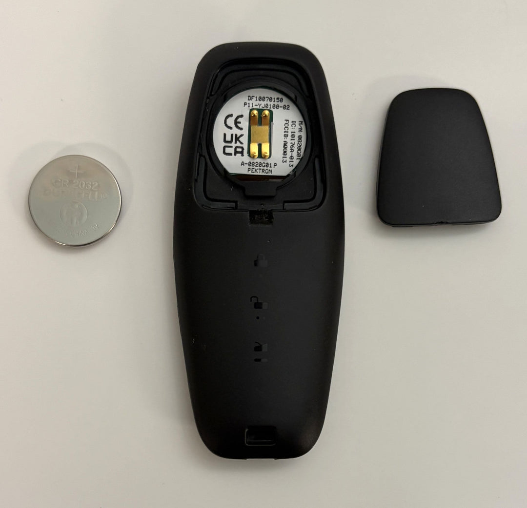 Disassembled Lucid Air key fob showing black plastic casing, internal circuit with visible FCC information, and a round silver battery on a white background.