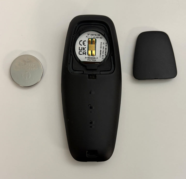 Disassembled Lucid Air key fob showing black plastic casing, internal circuit with visible FCC information, and a round silver battery on a white background.