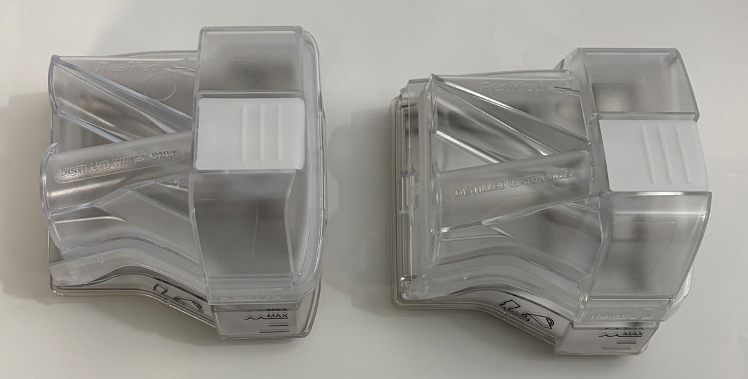 Two clear molded plastic replacement water chambers designed by Resmed for CPAP humidifiers, shown side by side on a plain surface.