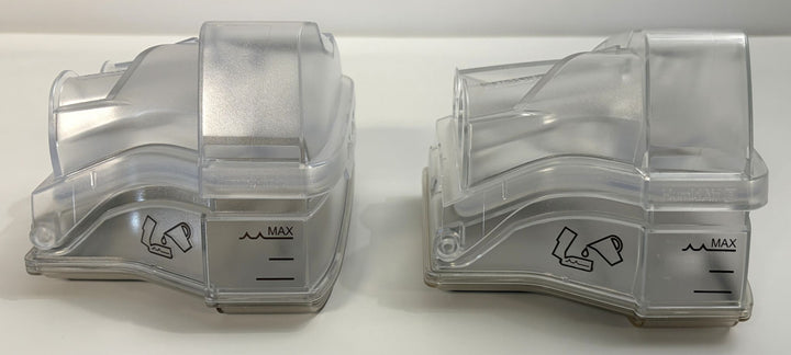Two clear plastic replacement water chamber tubs designed for Resmed CPAP humidifiers, featuring measurement markings and a compact, curved shape.