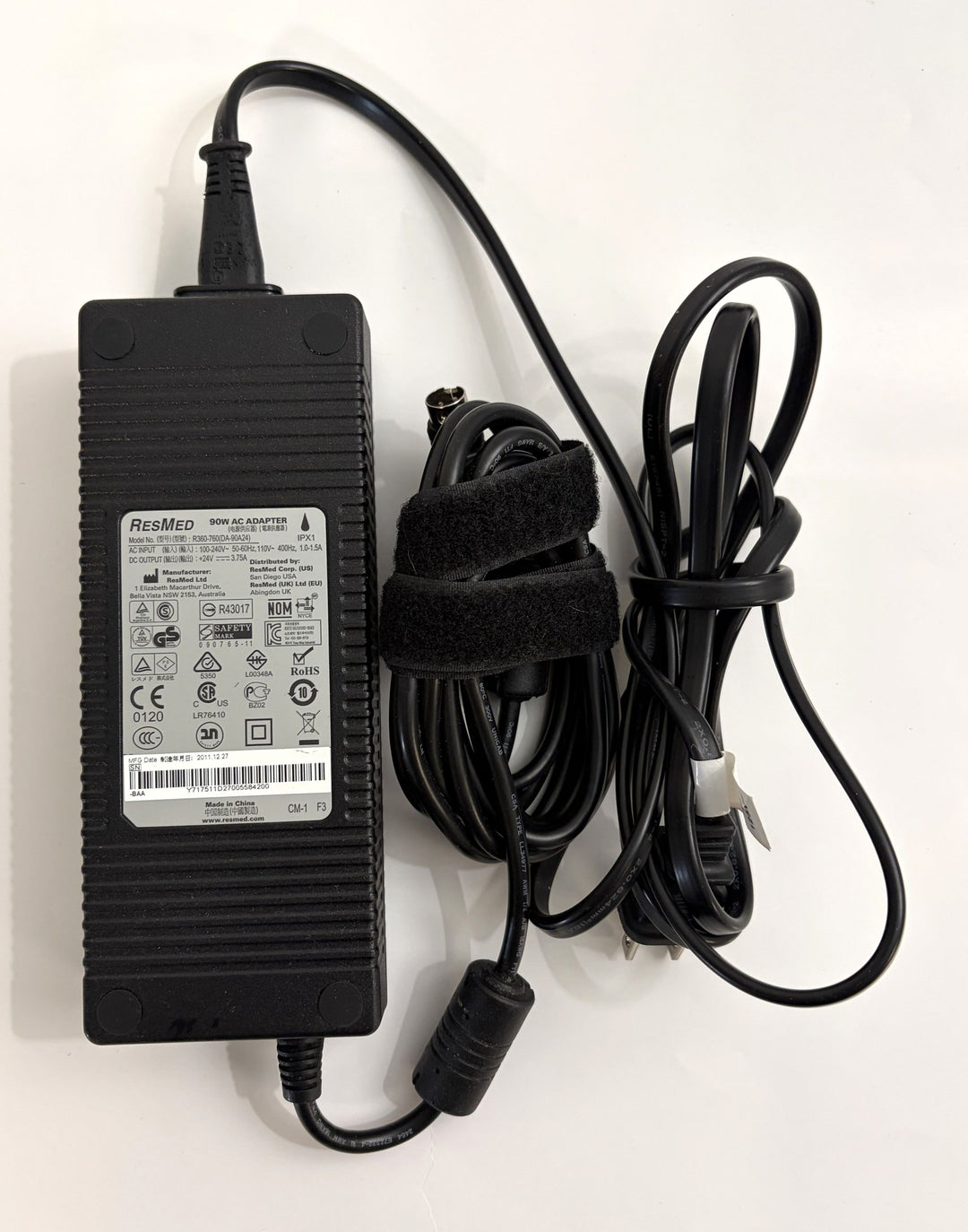 Pre-owned Resmed 90W AC adapter power supply with attached black cables, showing product label containing safety and certification symbols on a white background.