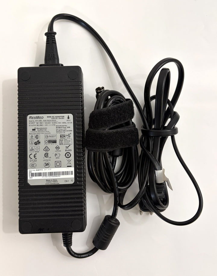 Pre-owned Resmed 90W AC adapter power supply with attached black cables, showing product label containing safety and certification symbols on a white background.