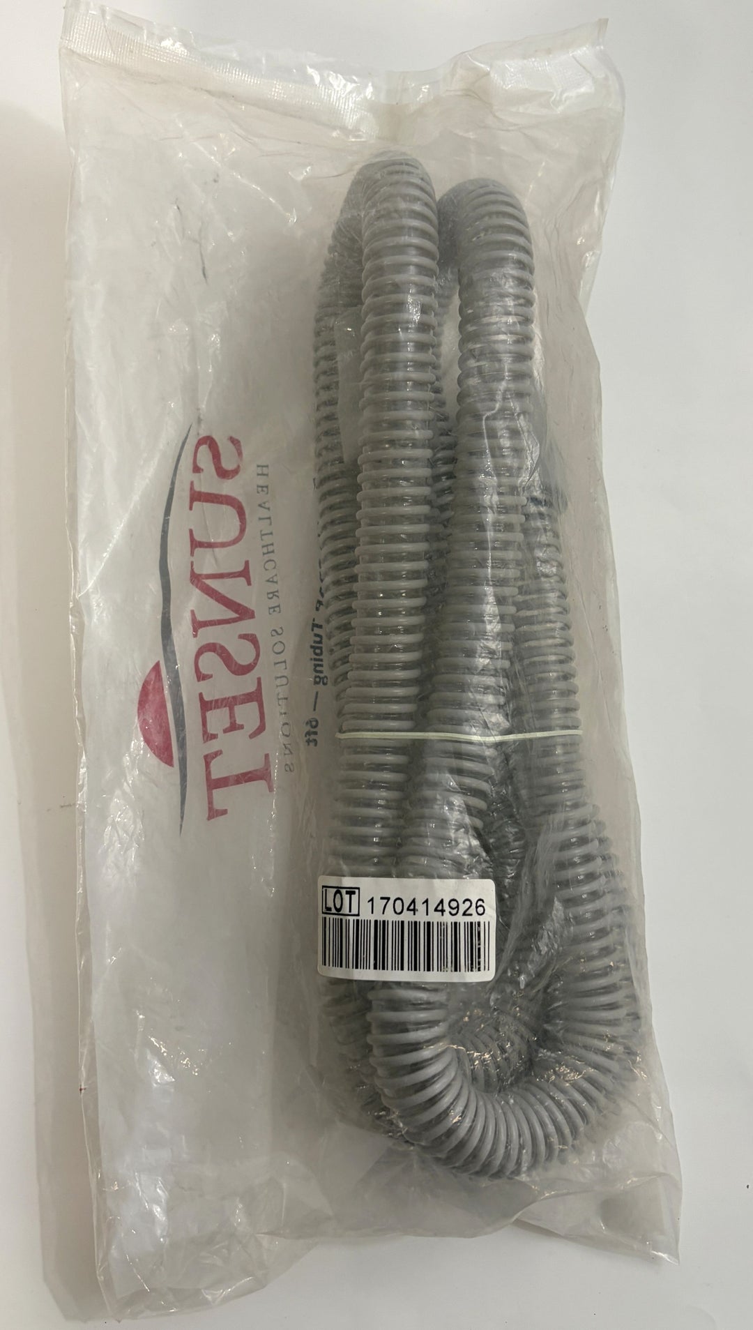 Factory-sealed gray flexible CPAP hose from Sunset Healthcare Solutions, coiled inside clear plastic packaging with visible lot and barcode label.