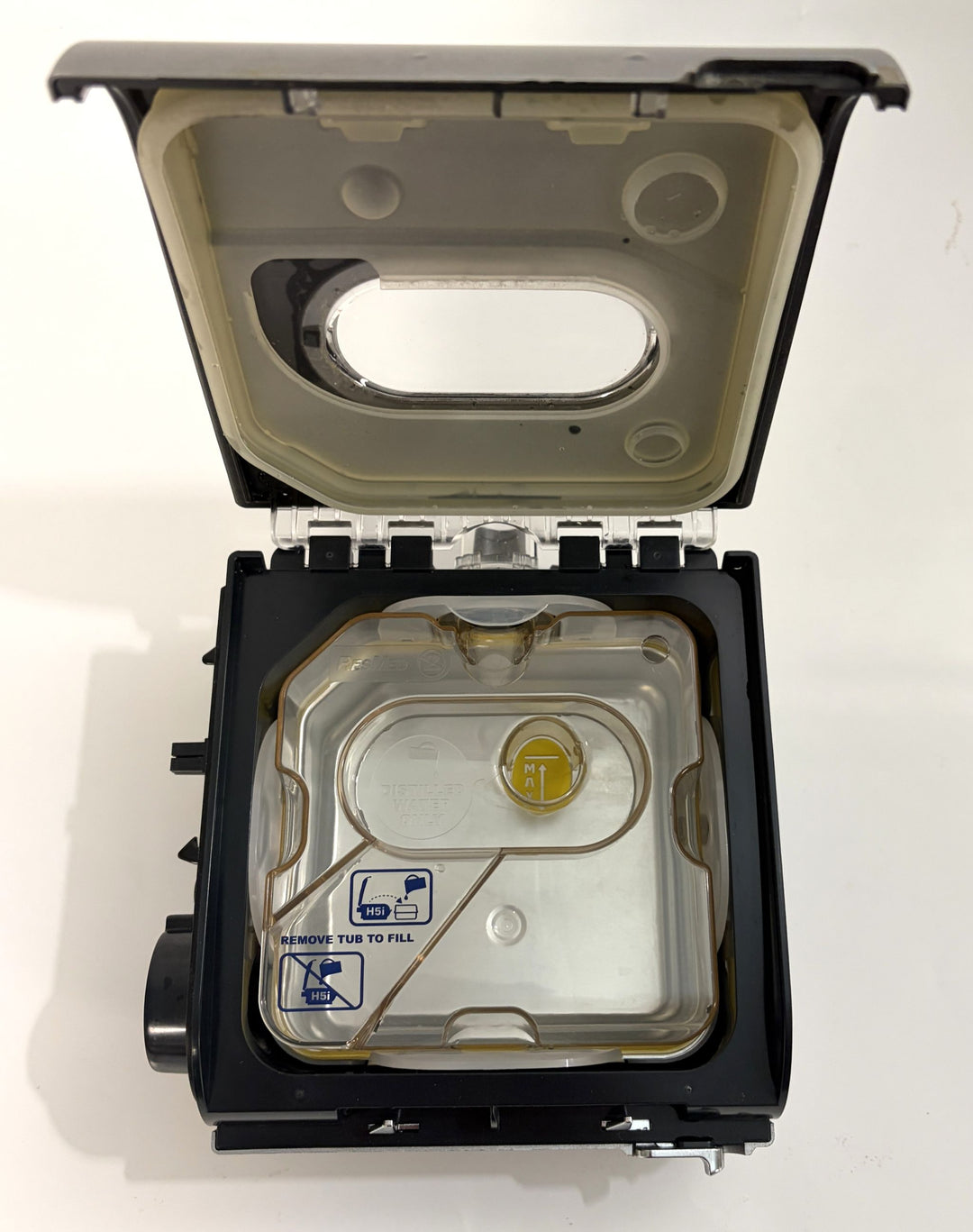Open Resmed H5i humidifier component with visible water reservoir and fill instructions on a clear plastic lid, showing internal design for medical device use.