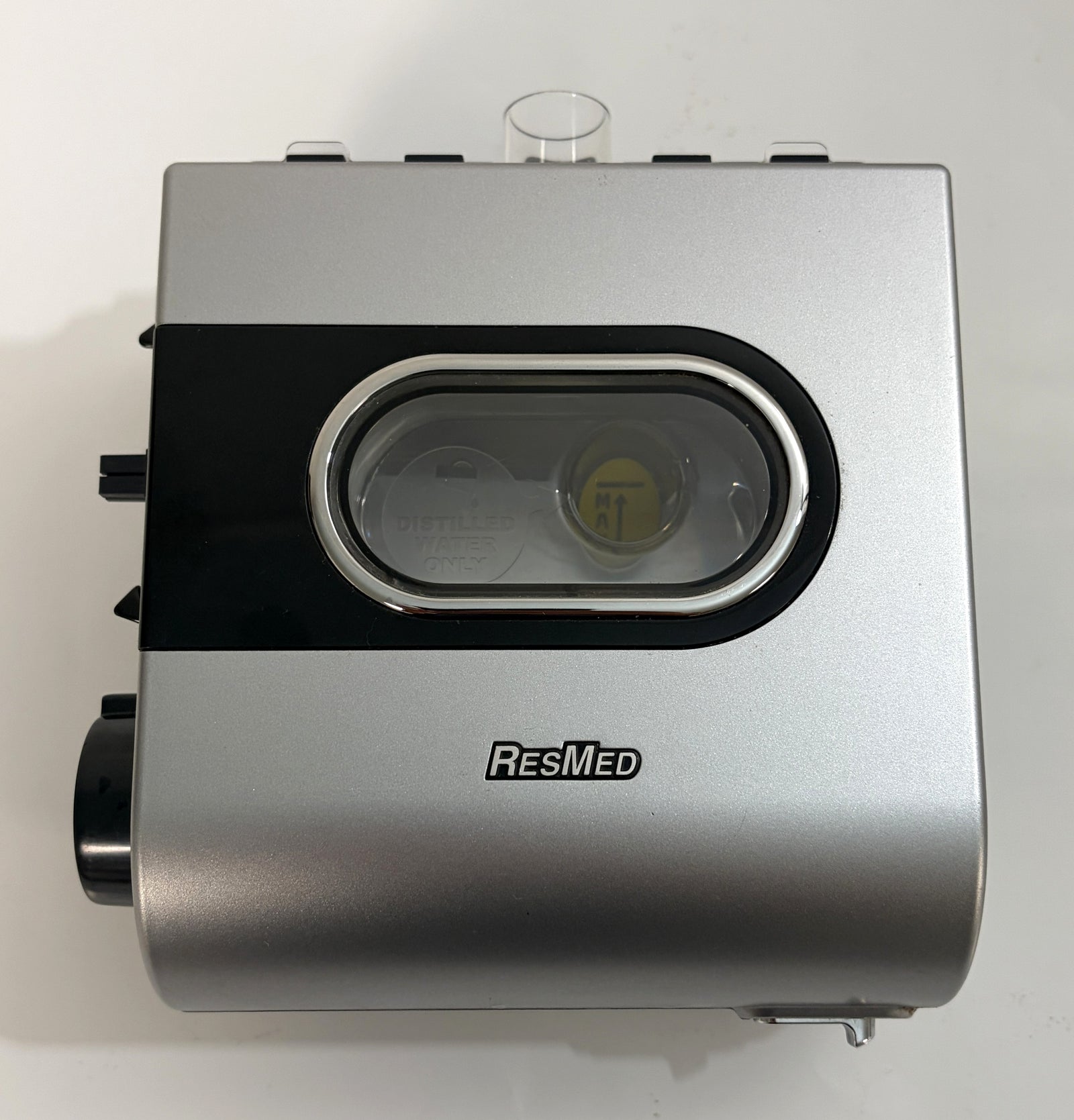 Silver and black Resmed humidifier component with clear water chamber window and visible internal yellow float valve, designed for CPAP devices.