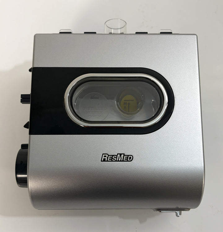 Silver and black Resmed humidifier component with clear water chamber window and visible internal yellow float valve, designed for CPAP devices.