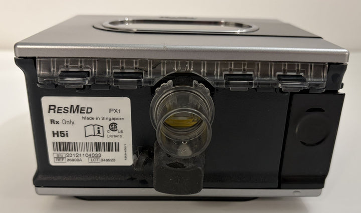 Close-up of a ResMed H5i humidifier component showing the front water chamber port and label indicating model details and manufacturing origin.