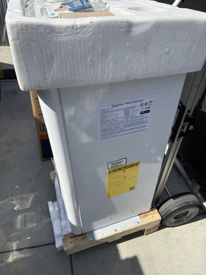 White household appliance secured on a wheeled hand truck, wrapped with protective foam and displaying safety and EnergyGuide labels.