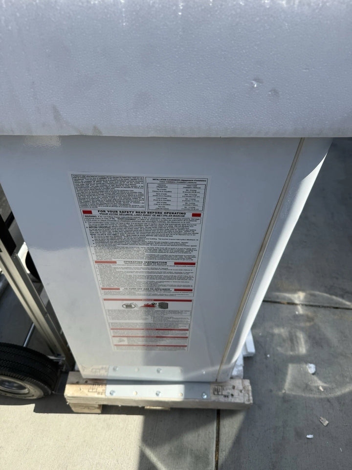 White metal equipment housing with a large safety instruction label, support frame, and wheel visible on a concrete surface.