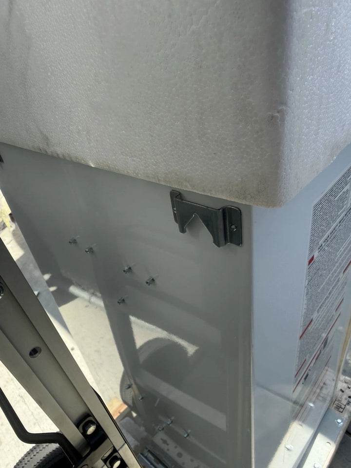 Close-up of a gray metal equipment panel with black mounting brackets, white textured insulation, metal rails, and a partially visible warning label.