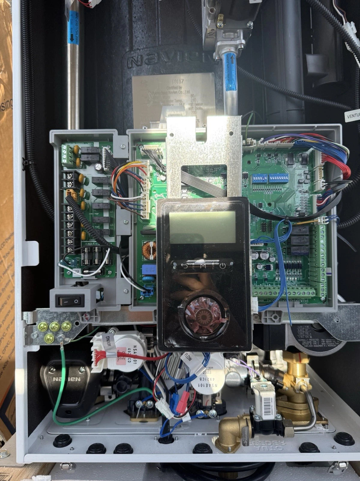 Open industrial electrical control cabinet showing circuit boards, wiring, digital display, sensors, pipes, valves, and mechanical components inside.