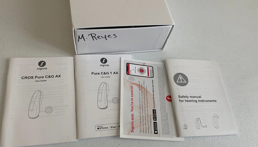 Packaging of hearing instruments with manuals and safety information on a light gray background