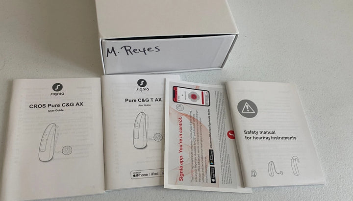 Packaging of hearing instruments with manuals and safety information on a light gray background