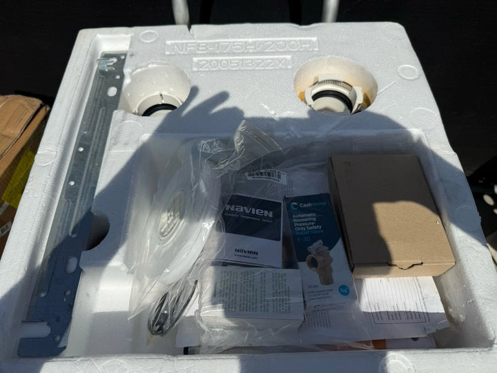 White molded foam packing insert containing wrapped components, instruction papers, a Navien booklet, and a small brown cardboard box.