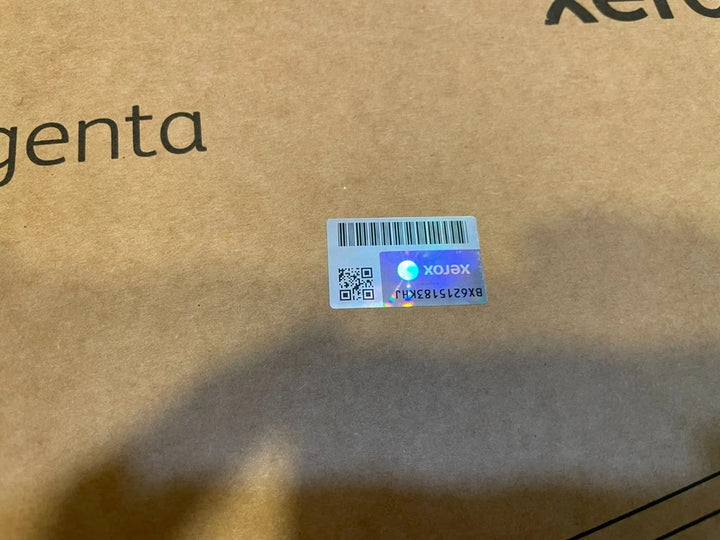 Close-up of a brown cardboard box featuring a holographic Xerox security label and partial printed text indicating magenta toner, sourced from PHENTERSALES for industrial and business use.