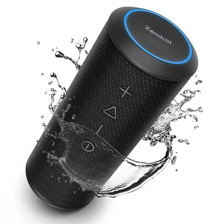Black Zamkol portable wireless Bluetooth speaker with IPX6 waterproof rating, control buttons on fabric surface, blue LED ring, and water splashing to show durability.